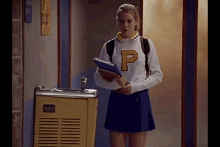a girl in a cheerleader uniform is standing in front of a water fountain holding a notebook .