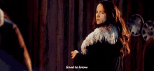 a woman in a fur coat is standing in front of a wooden wall and talking to someone .