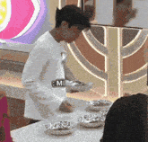 a man in a white shirt is standing in front of a table with bowls of food and a sign that says mi