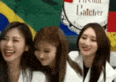 three women are sitting next to each other and smiling in front of a flag .