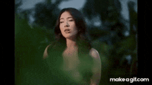 a woman in a white top is standing in front of a tree .