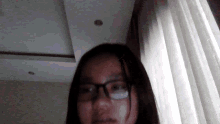 a woman wearing glasses is standing in front of a white curtain
