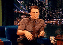 a man in a plaid shirt and tie sitting in a chair