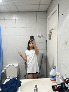 a woman taking a selfie in a bathroom with a bottle of bleach on the counter