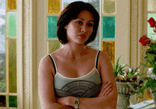 a woman in a tank top is standing with her arms crossed in front of a window