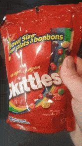 a person is holding a bag of skittles with a bite taken out of it