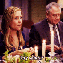 a man and a woman are sitting at a table with candles and the woman is saying " say what "