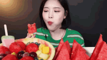 a woman is eating a slice of watermelon from a plate of fruit