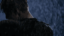 a man in a black shirt is standing in the rain with his head down .