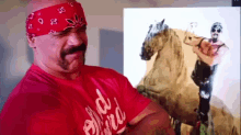 a man with a bandana on his head is standing in front of a picture of a man on a horse .
