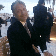 a man in a suit and tie is sitting in a chair and making a face .