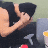 a man wearing a black tank top and a black beanie is sitting at a table with his head down .
