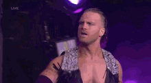 a wrestler is standing in a dark room with a purple background and looking at the camera .