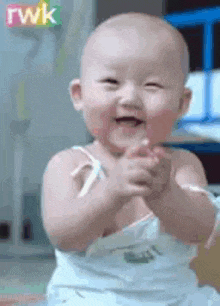 a baby is clapping his hands and smiling while wearing a diaper .
