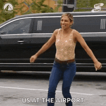 a woman in a tank top and jeans is dancing in front of a car .
