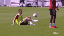 a man is sitting on the grass with his legs crossed while a soccer player kicks the ball .