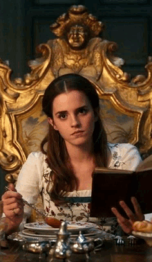 a woman is sitting at a table reading a book while holding a fork .