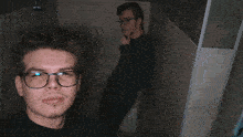 a man wearing glasses is taking a selfie with another man behind him