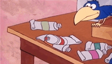 a cartoon bird is looking at a table full of tubes of paint .
