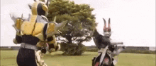two kamen riders are fighting in a field with a tree in the background .