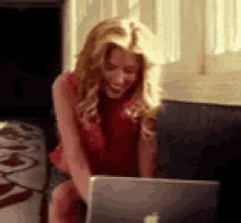 a woman in a red shirt is sitting in front of a laptop computer .