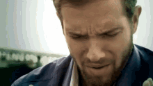 a close up of a man 's face with a beard wearing a blue shirt