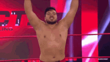 a shirtless wrestler is hanging upside down in a wrestling ring with his arms in the air .