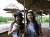 two women are standing next to each other under a roof with thatched umbrellas .