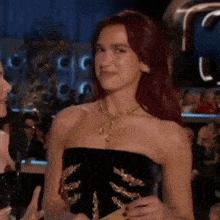 a woman with red hair is wearing a black strapless dress and a gold necklace while holding a piece of paper .