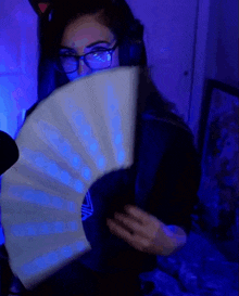 a woman wearing glasses is holding a white fan in front of her face .