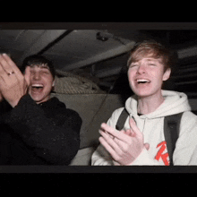 two young men are laughing and clapping in a dark room
