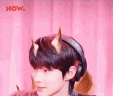 a young man wearing headphones and horns on his head is standing in front of a pink curtain .