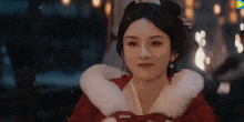 a woman in a red dress with a white fur collar is smiling .