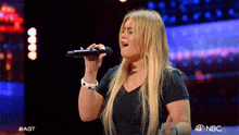 a woman singing into a microphone with nbc behind her