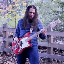 a man with long hair is playing a red electric bass guitar