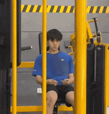 a man in a blue adidas shirt is sitting on a machine in a gym