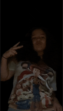 a girl wearing a toy story t-shirt is giving a peace sign in the dark