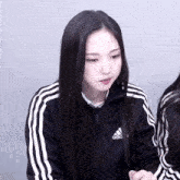 a girl wearing a black adidas jacket with white stripes on the sleeves