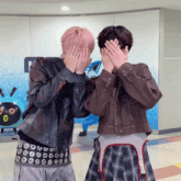 two people covering their faces with their hands in front of a wall with the letter t on it