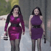 two women wearing purple dresses are walking down a street .