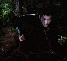 a man in a black and red outfit is kneeling down in the woods