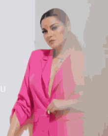 a woman wearing a pink jacket with a plunging neckline is standing in front of a white wall