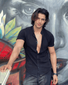 a man in a black shirt is standing in front of a painting of a woman 's face