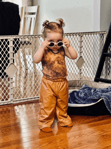 a little girl wearing brown leather pants and sunglasses
