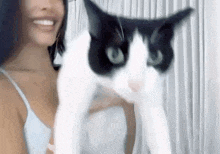 a woman is holding a black and white cat with green eyes in her arms .