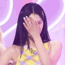 a woman covering her face with her hand while wearing a yellow top