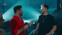 two men are standing next to each other on a stage holding microphones .