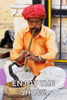 a man wearing a red turban is playing a snake pipe with the words enjoy the show below him