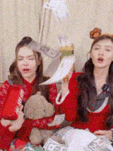 two women are throwing money in the air while sitting at a table with a teddy bear .
