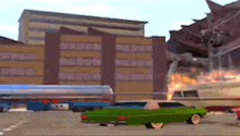 a green car is driving down a street in front of a building with fire coming out of it .